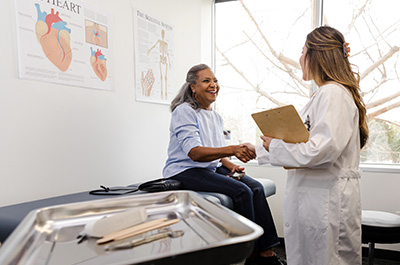woman sitting on exam table shaking hands with a female doctor