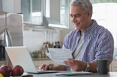 man sitting in the kitchen on computer paying bills