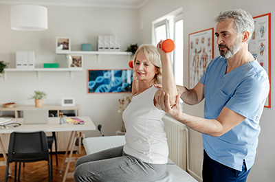 older women lifting weights with assistance of a physical therapist