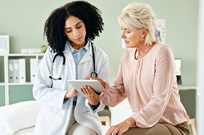 Female doctor sitting with an older female patient looking at a computer tablet