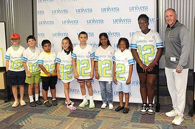eight children in football jerseys standing next to Paul Valley, Univera Healthcare president