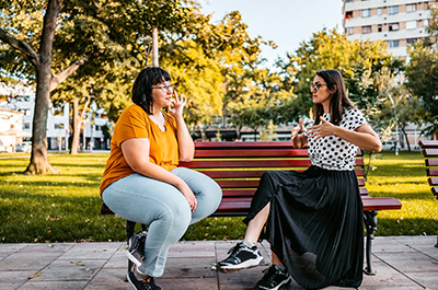 two women sitting outside on a bench talking in sign language